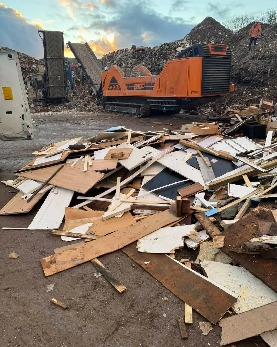 Waste wood tipped at a recycling site with a shredder behind